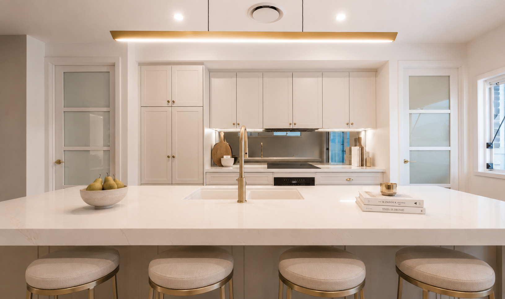 Bright modern kitchen with white island, brass faucet, bar stools, and mirrored backsplash