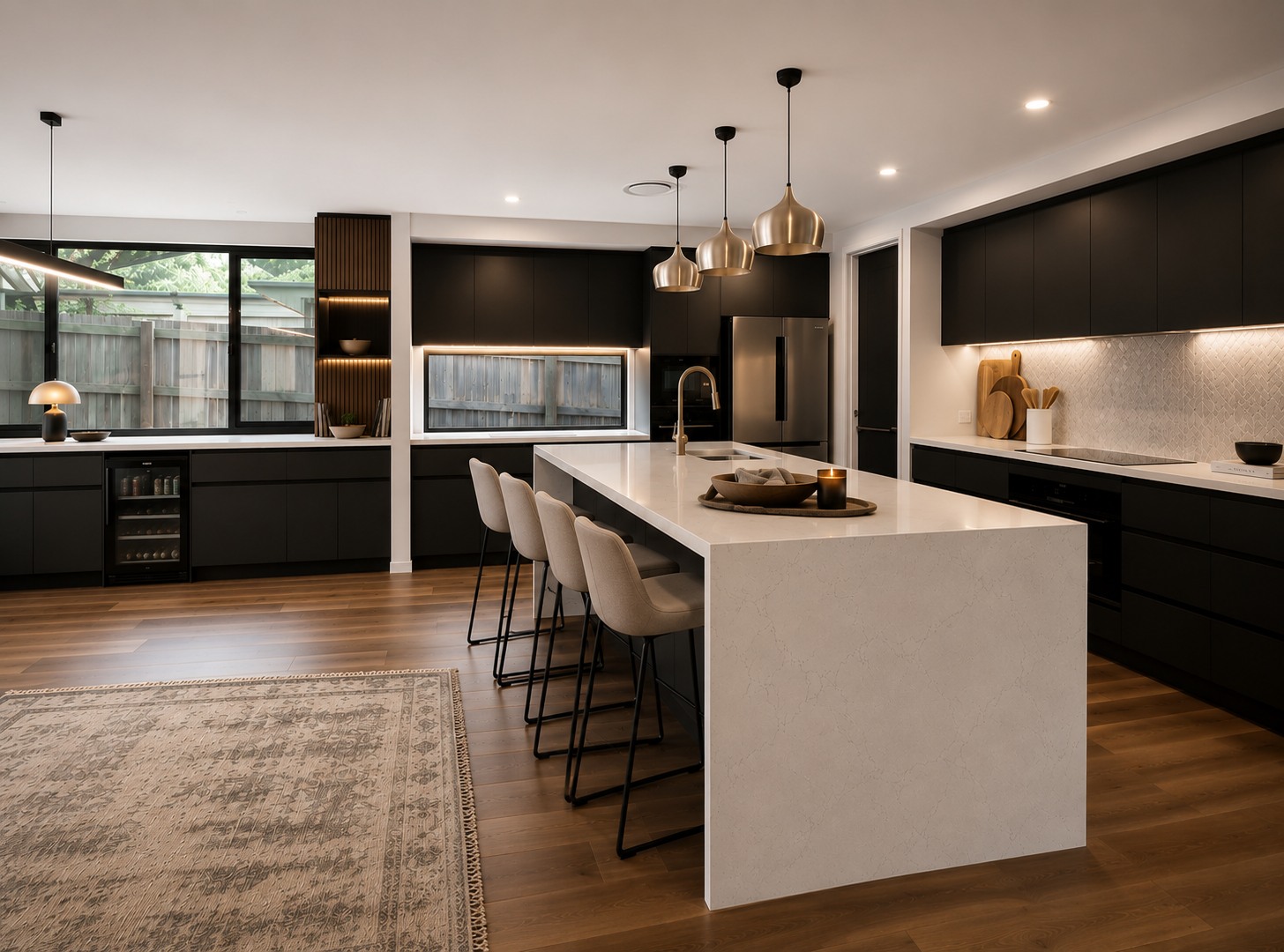 Modern open-concept kitchen with a white island, dark cabinets, and wood floors in warm lighting