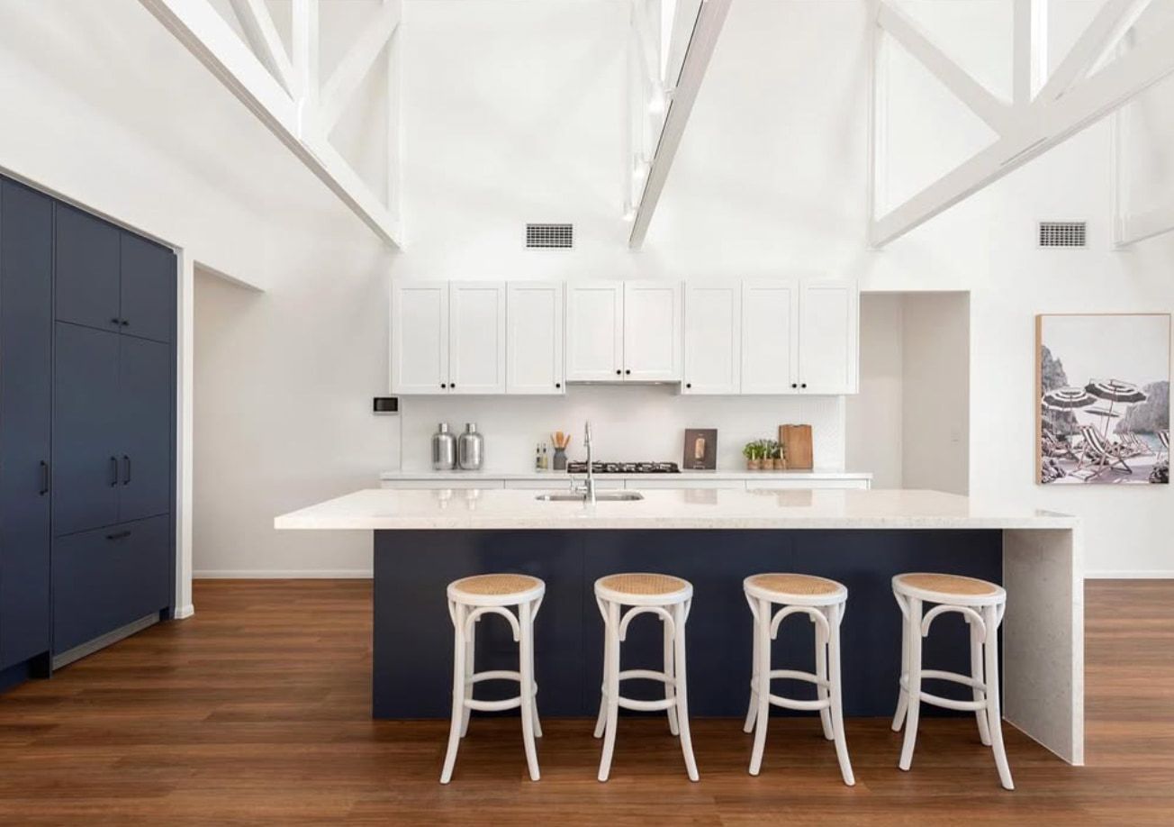 Bright modern kitchen with white cabinets, dark island, and four white stools