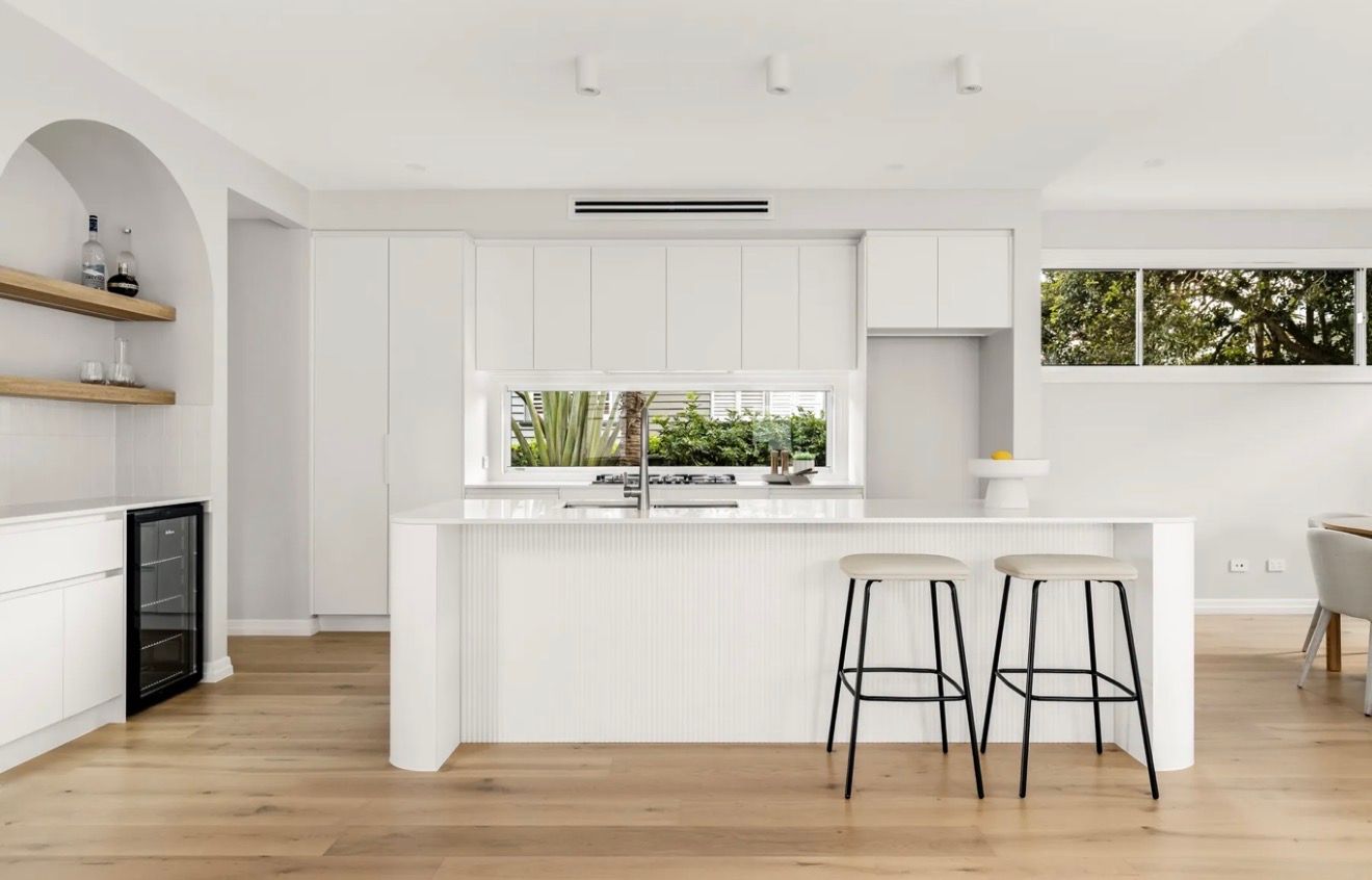 Bright white modern kitchen with island, bar stools, wooden floors, and large windows