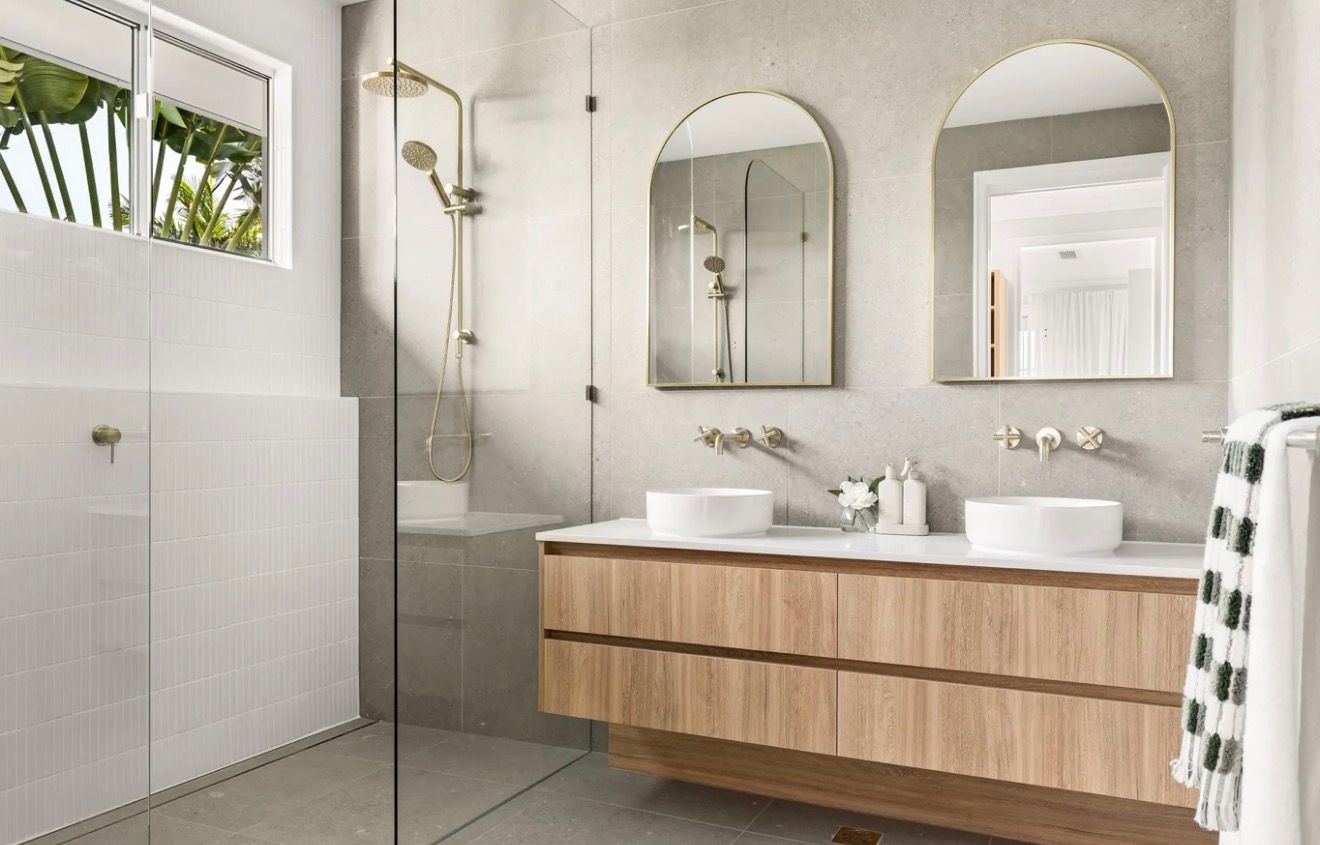 Modern bathroom with wood vanity, dual sinks, mirrors, shower, and a window with plants