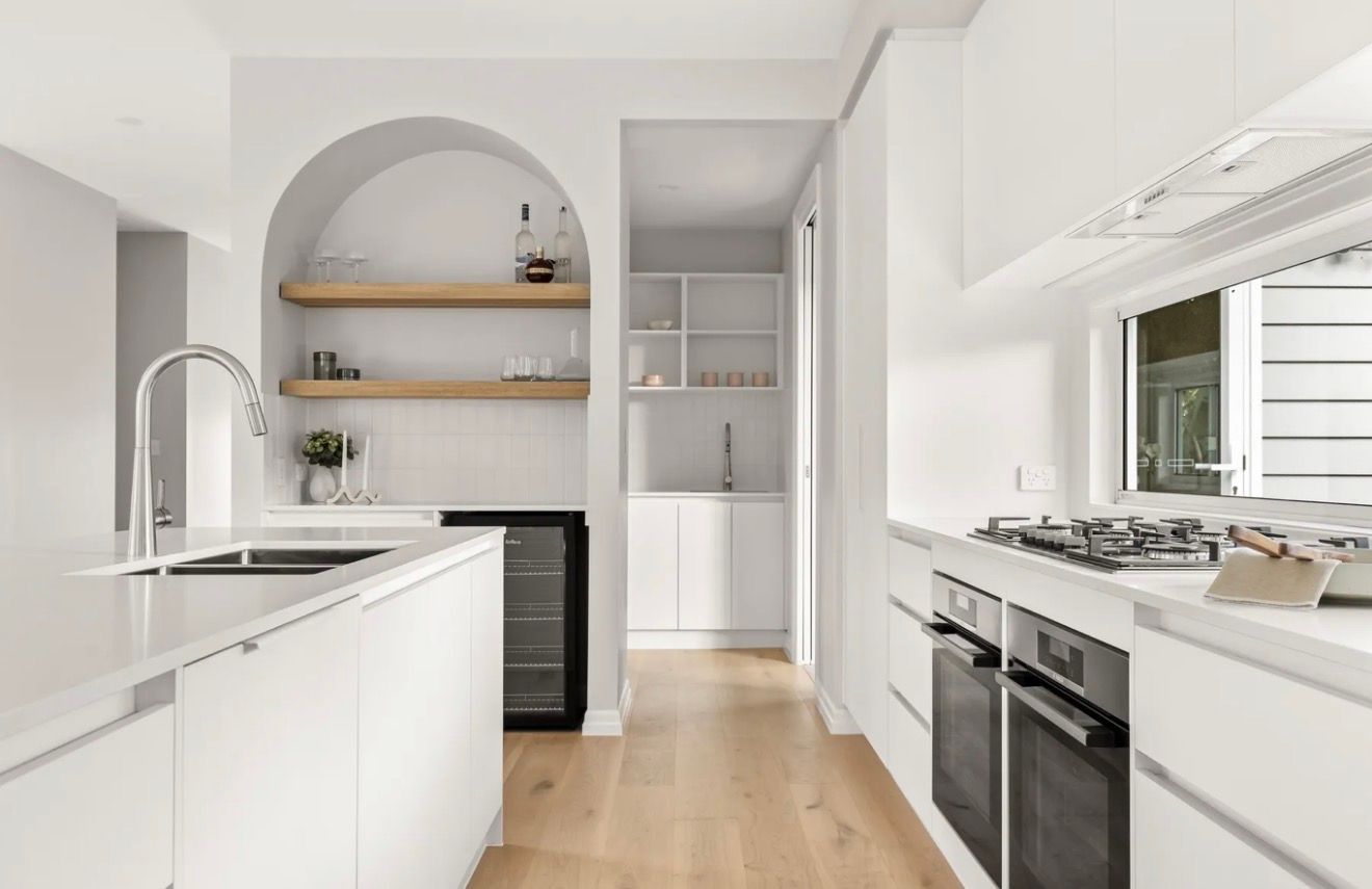 Bright modern white kitchen with island, arched shelving, and stainless steel appliances