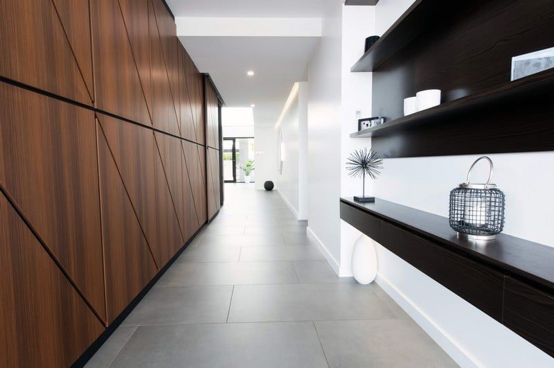 Modern hallway with wood-paneled wall, gray floor tiles, and black floating shelves on the right.