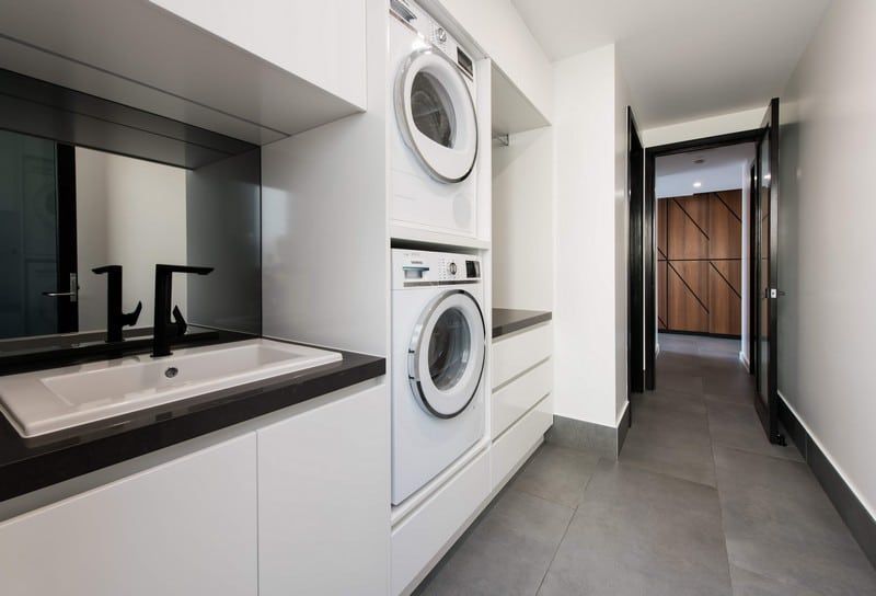 Modern laundry hallway with stacked washer and dryer, black countertops, and gray tile floor.