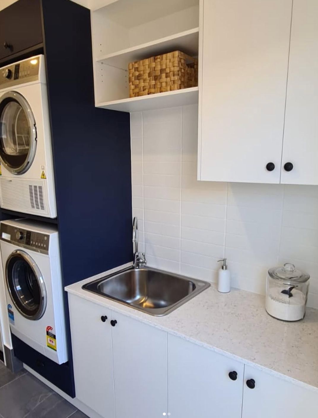 Laundry room with stacked washer and dryer, sink, white cabinets, and wicker basket on shelf