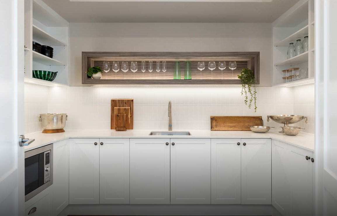 Bright modern white kitchen with open shelving, wood accents, and a long counter beneath a serving niche