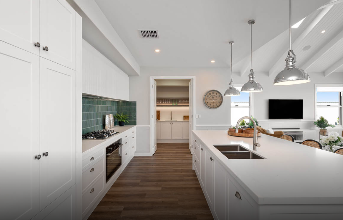 Bright modern white kitchen with island, pendant lights, wood floors, and a view to another room.