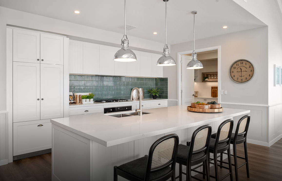 Bright modern kitchen with white island, pendant lights, teal backsplash, and black bar stools.