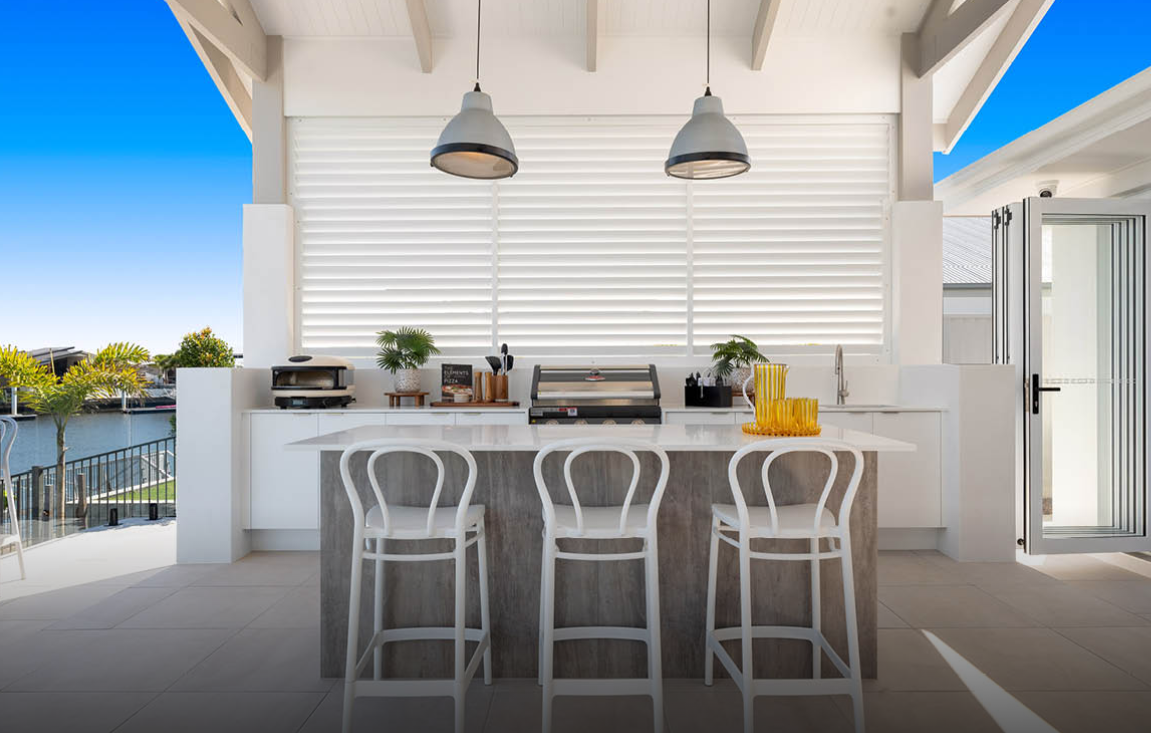 Modern white outdoor kitchen with bar stools, pendant lights, and a view of the water