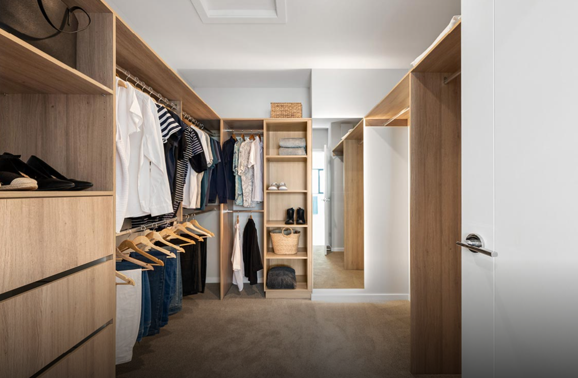 Walk-in closet with clothes, shelves, drawers, and an open door leading to a hallway.
