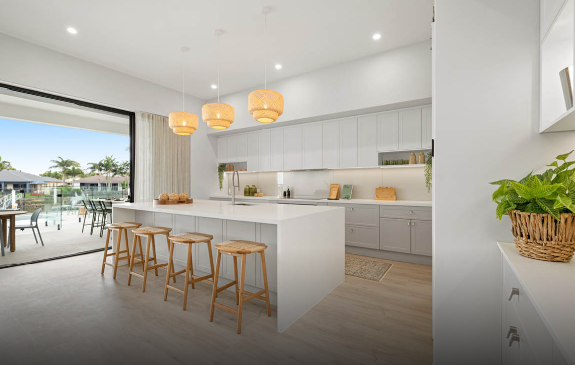 Modern white kitchen with island, wooden stools, pendant lights, and sliding doors to a patio
