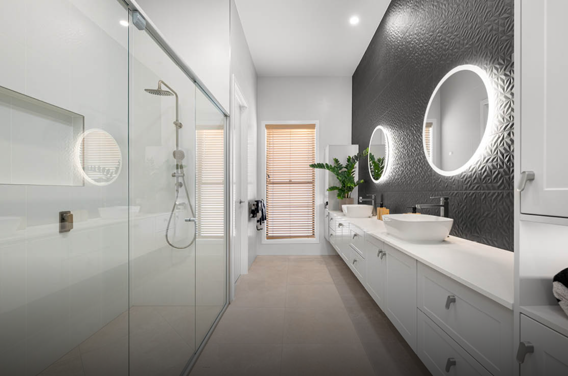Modern bathroom with glass shower, white vanity, round LED mirror, and gray tiled accent wall