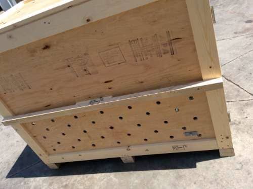 Wooden crate, light brown, with many holes, sitting on concrete.