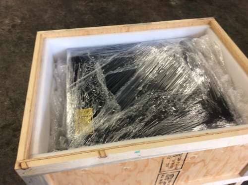 Object wrapped in plastic inside a wooden crate with foam padding.