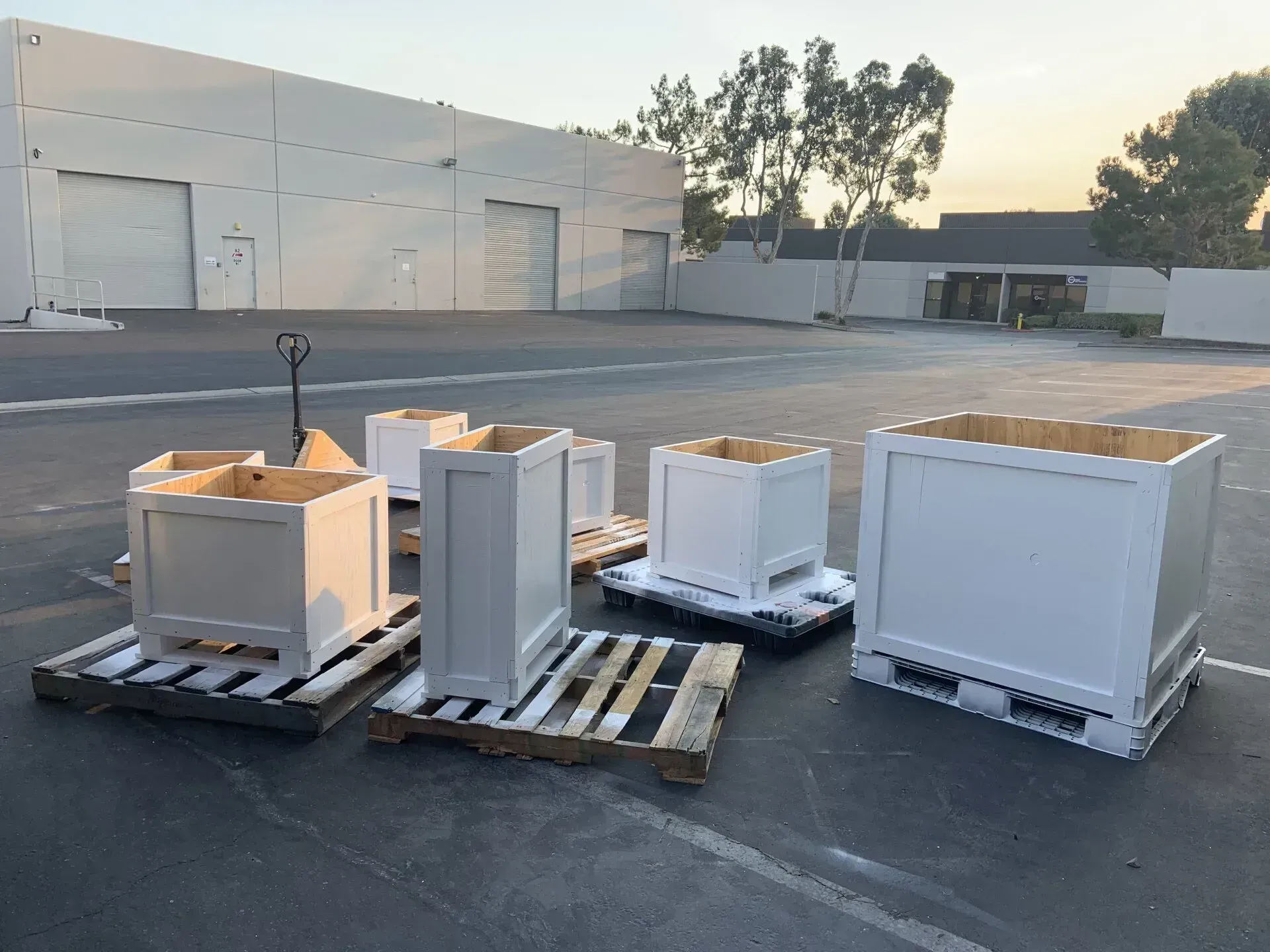 White planter boxes on wooden pallets in an outdoor lot in front of a building.