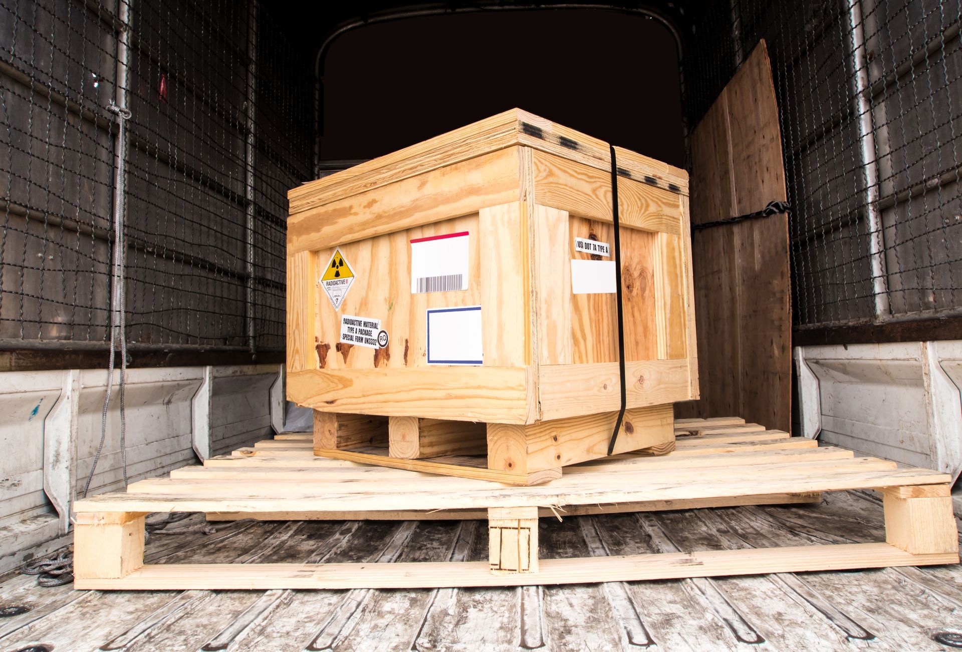 Wooden crate on pallet inside a truck, secured with black straps.