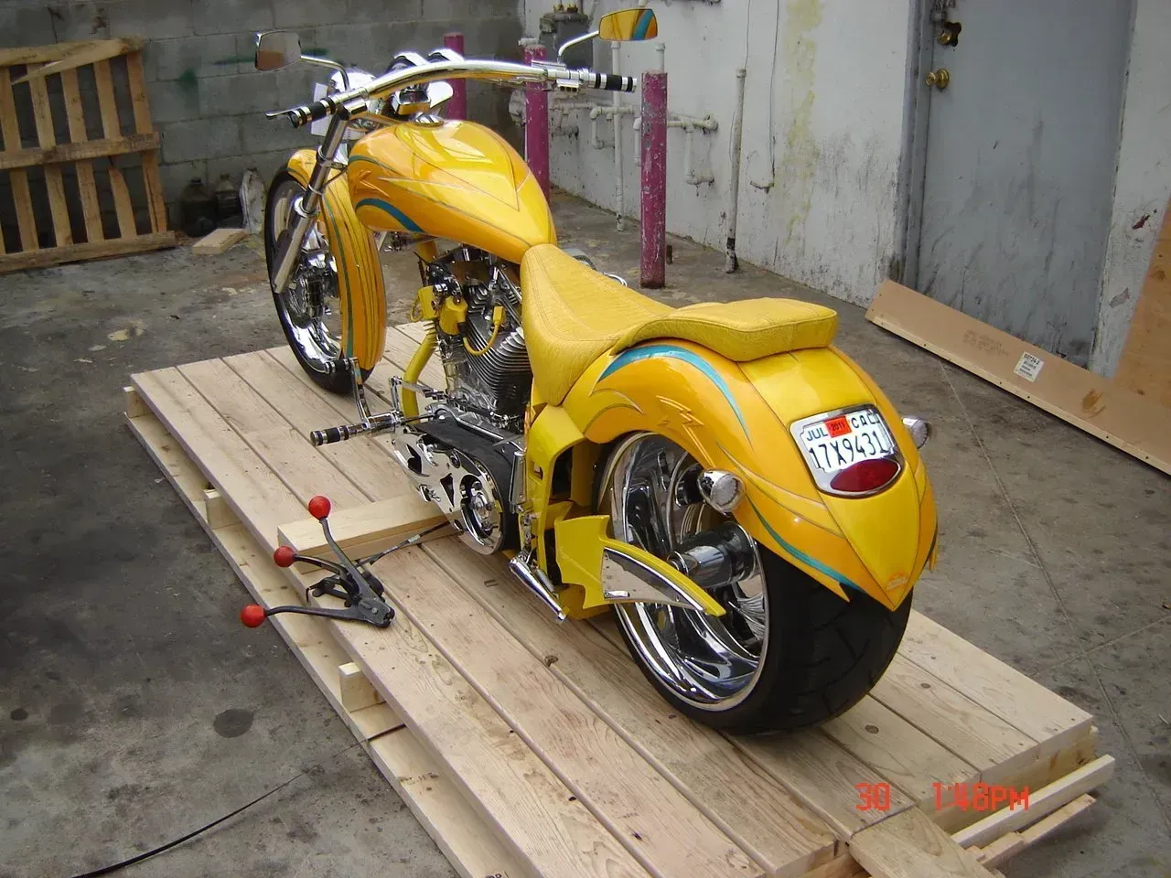 Yellow custom motorcycle on a wooden pallet, chrome accents, indoors.