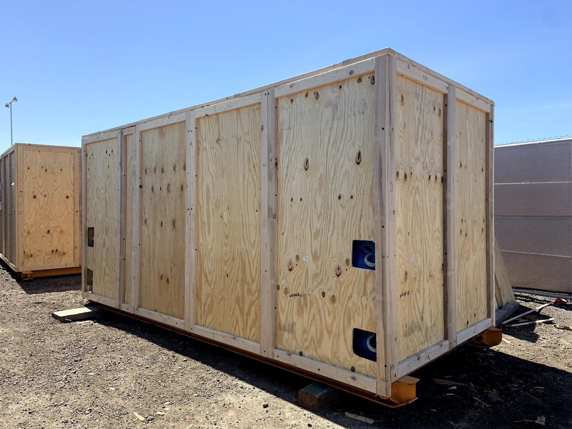 Wooden shipping crate on a pallet, outdoors on asphalt, bright sunlight.