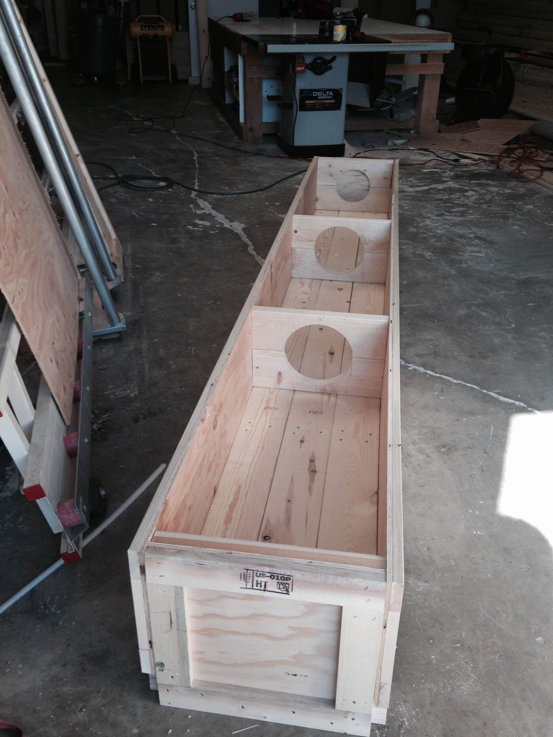 Wooden box with three circular cutouts and a hinged door in a workshop setting.