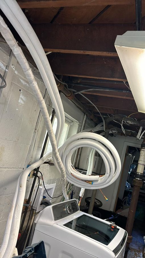 Coiled white tubing and a white appliance in a cluttered attic or utility space with exposed beams