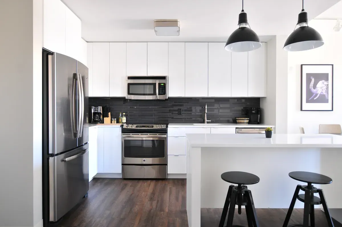 Modern kitchen with stainless steel appliances, white cabinets, dark backsplash, and a breakfast bar with stools