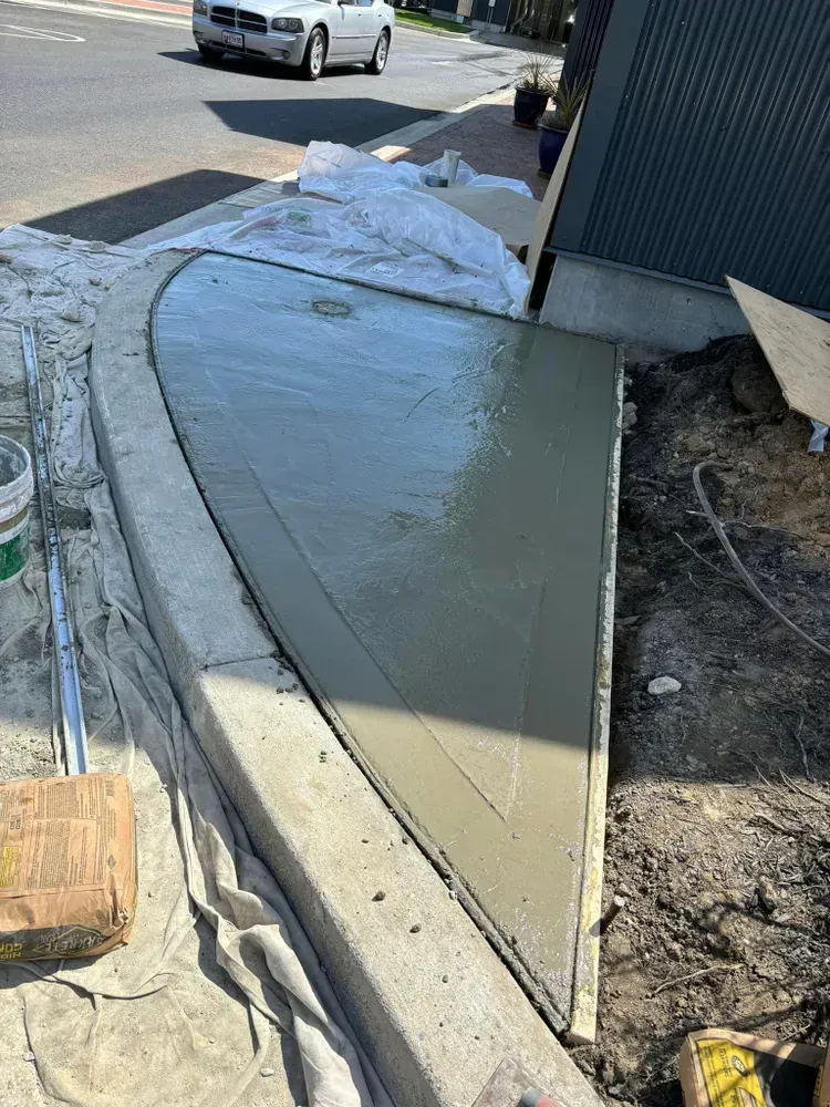 Fresh concrete sidewalk ramp corner beside a curb and street, with forms and construction debris nearby