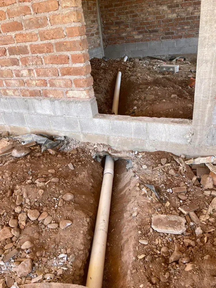 Construction trench with white pipe running from dirt ground into a brick building opening