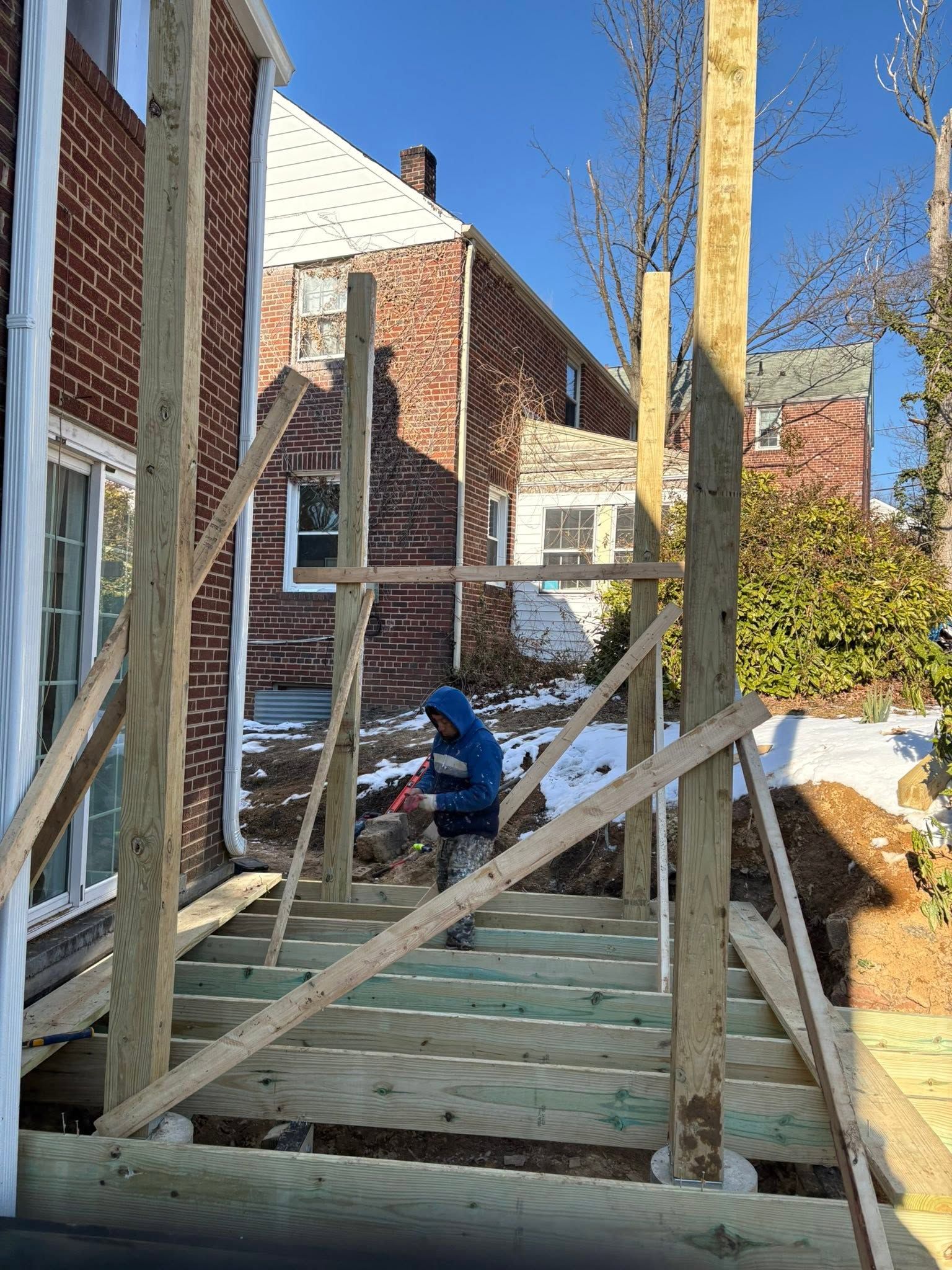 Partially built wooden porch deck beside a brick house with steps and rail framing under construction