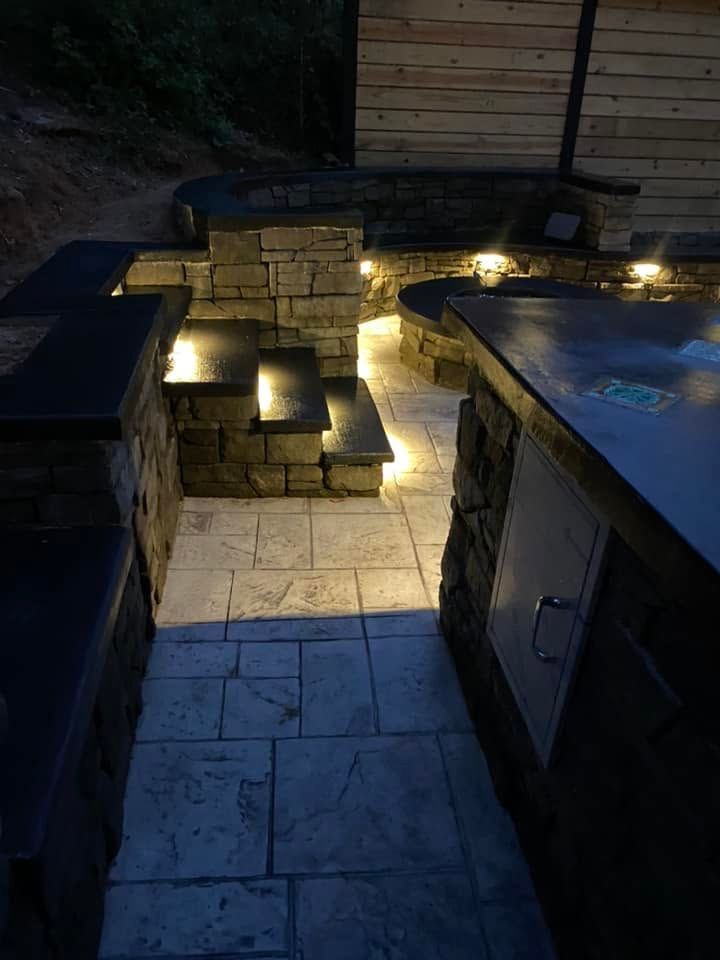 Backyard patio at dusk with stone steps, built-in seats, and warm step lights around a hot tub