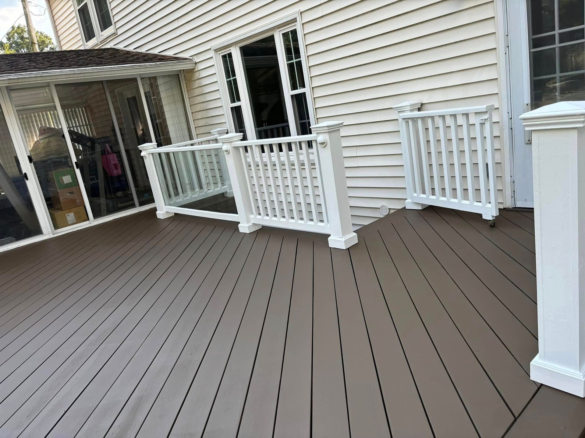 Wooden deck beside a house with white railings and sliding glass doors