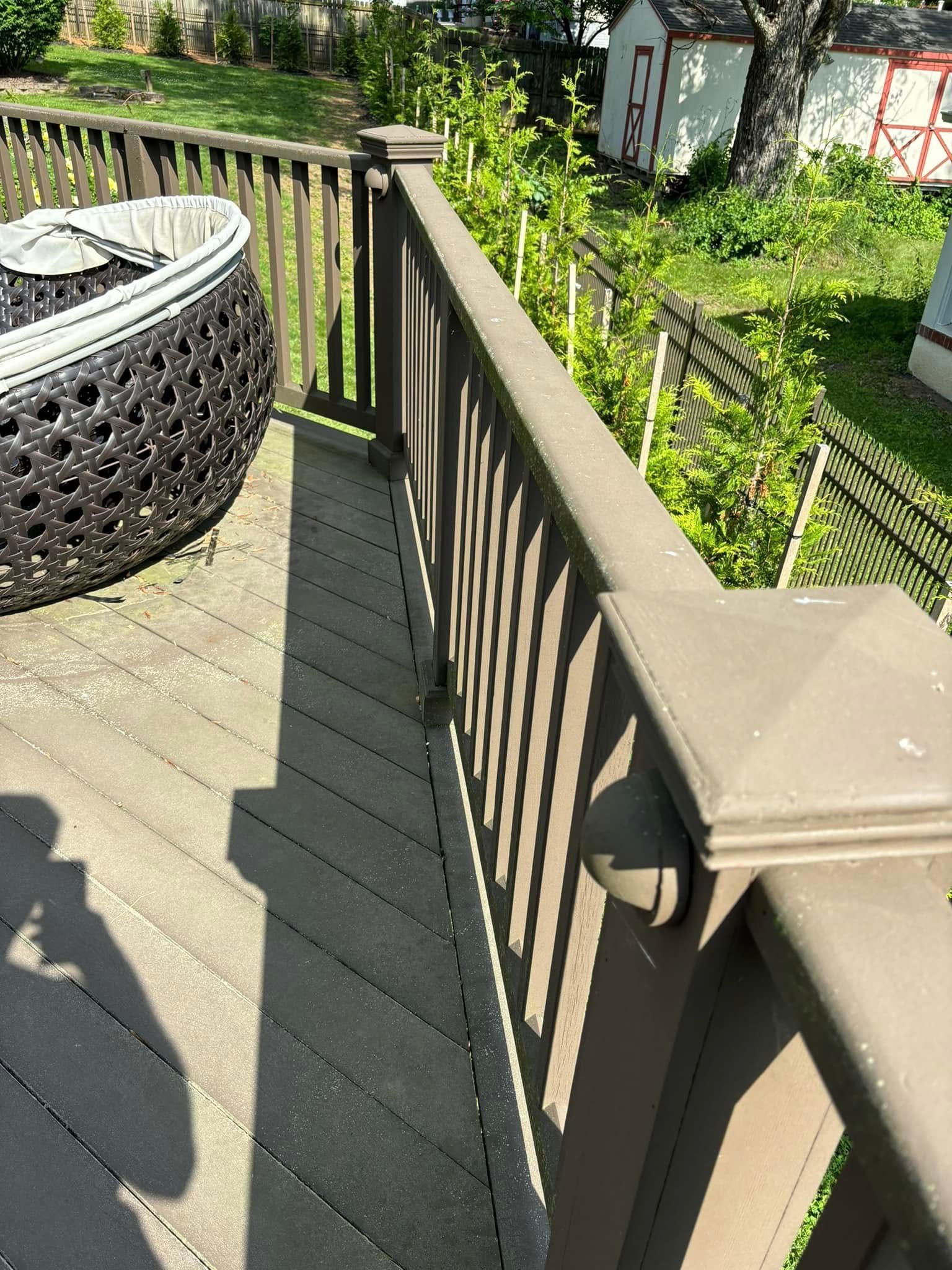 Backyard deck corner with tan railing, black wicker chair, and green garden beyond