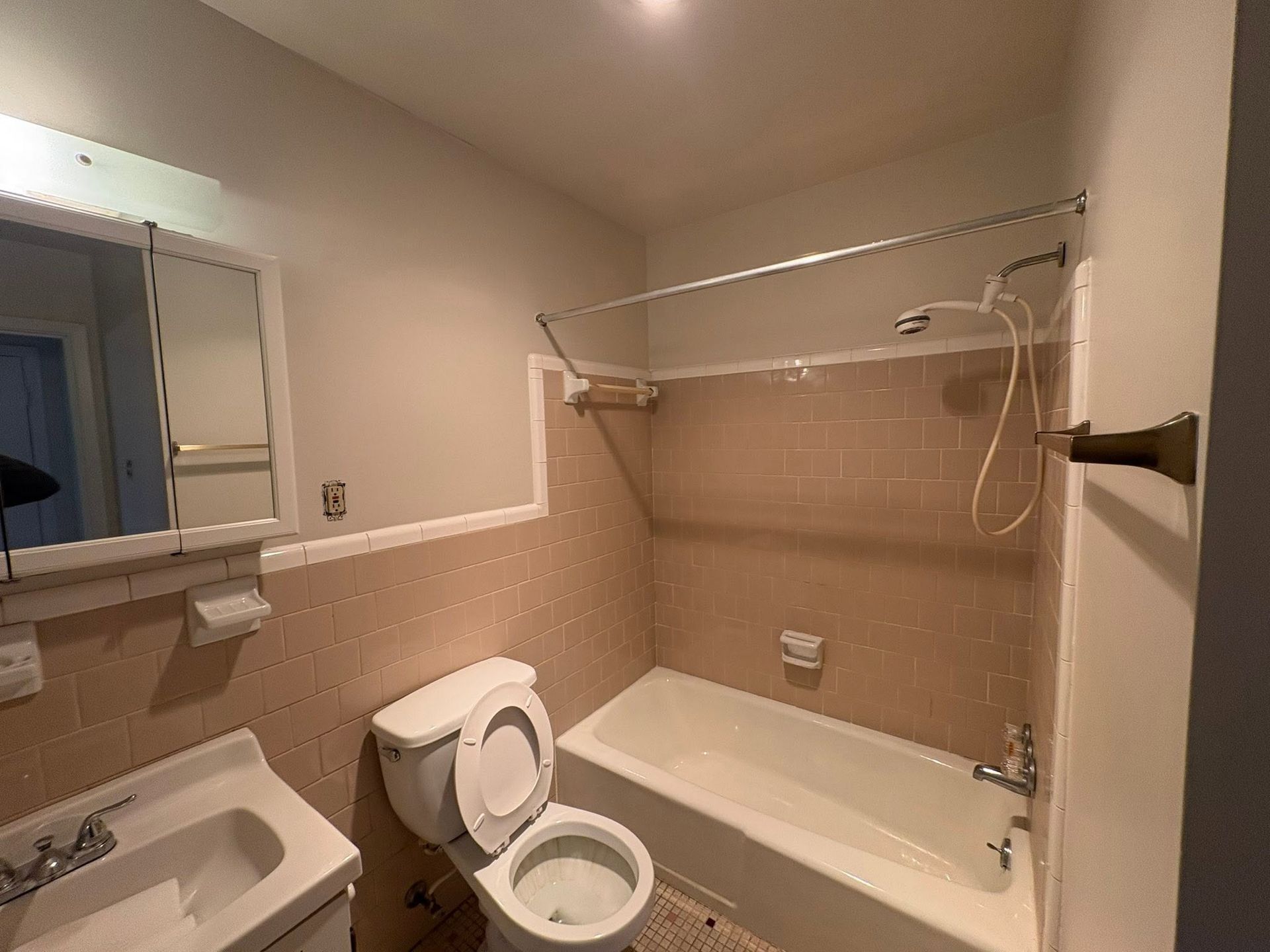 Small beige bathroom with sink, toilet, bathtub, mirror, and towel racks.