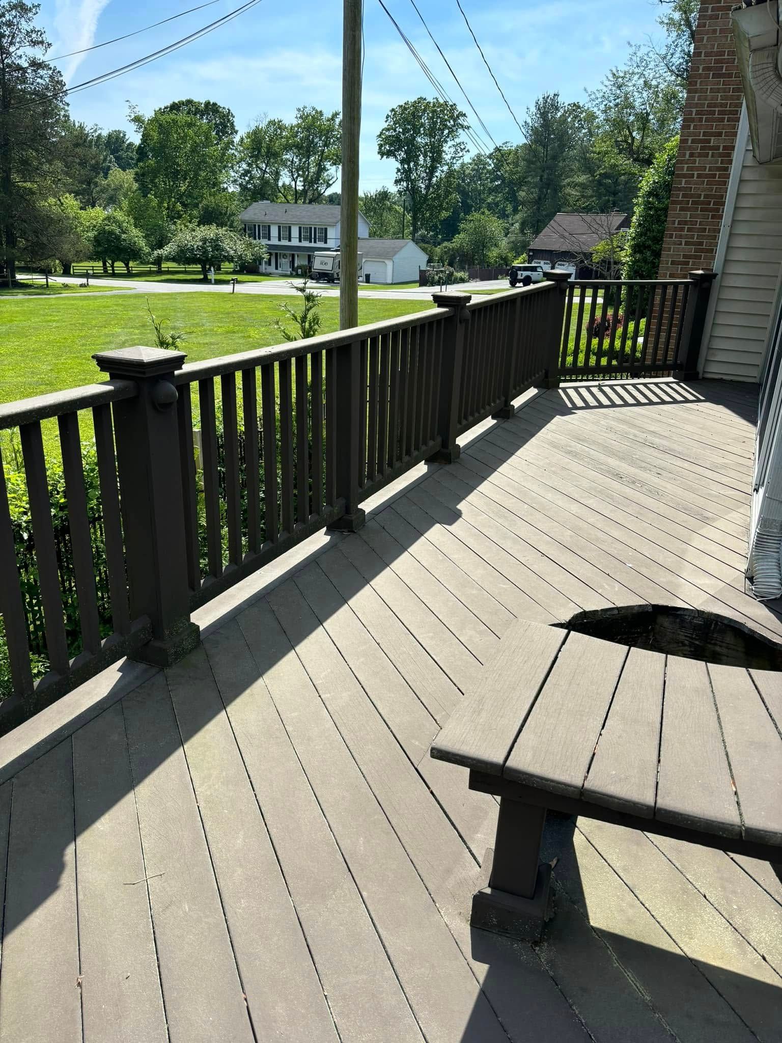 Sunlit wooden porch deck with railing overlooking a green yard and houses
