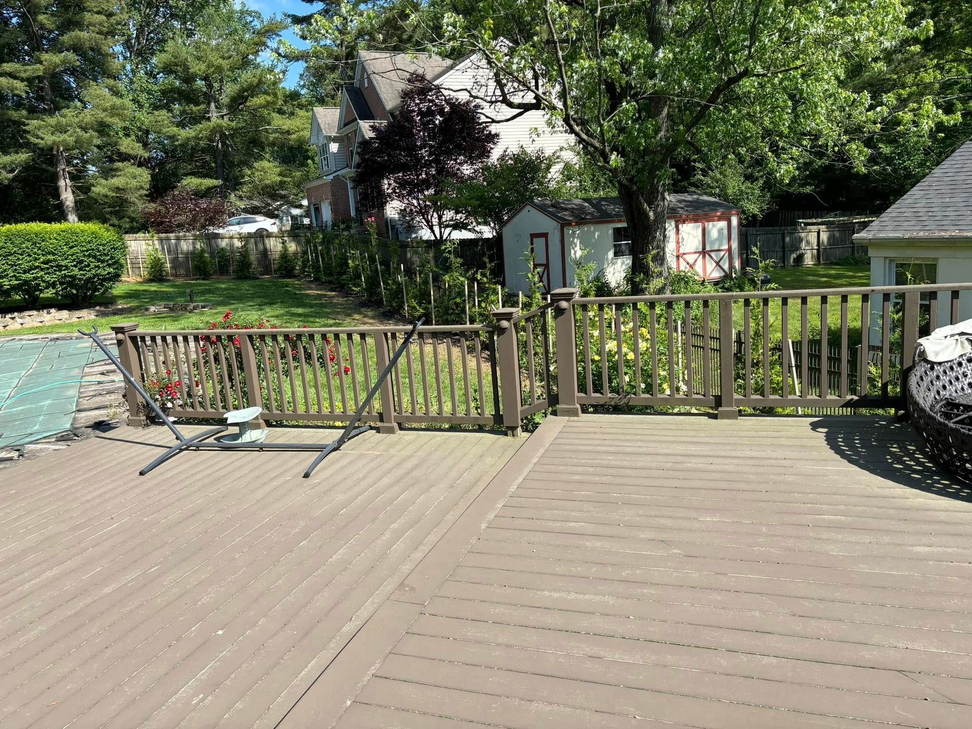 Wooden deck with railing, green lawn, and a backyard view with trees and house in the background