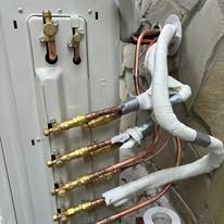 Outdoor HVAC refrigerant lines and valves wrapped in white insulation on a wall-mounted unit