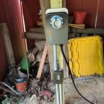 Utility box and meter on a post in a cluttered shed, with tools and a yellow bin nearby