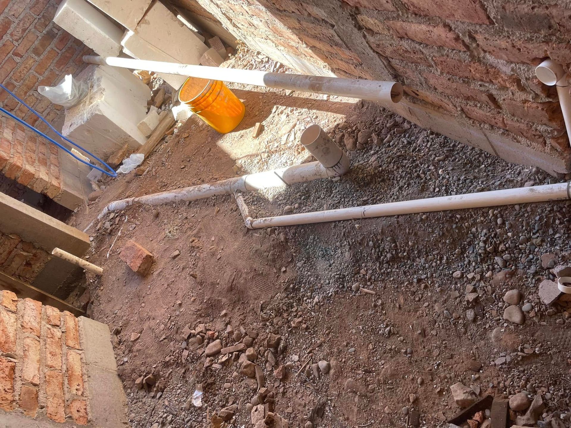 Construction site with dirt trench, pipes, and brick walls under renovation