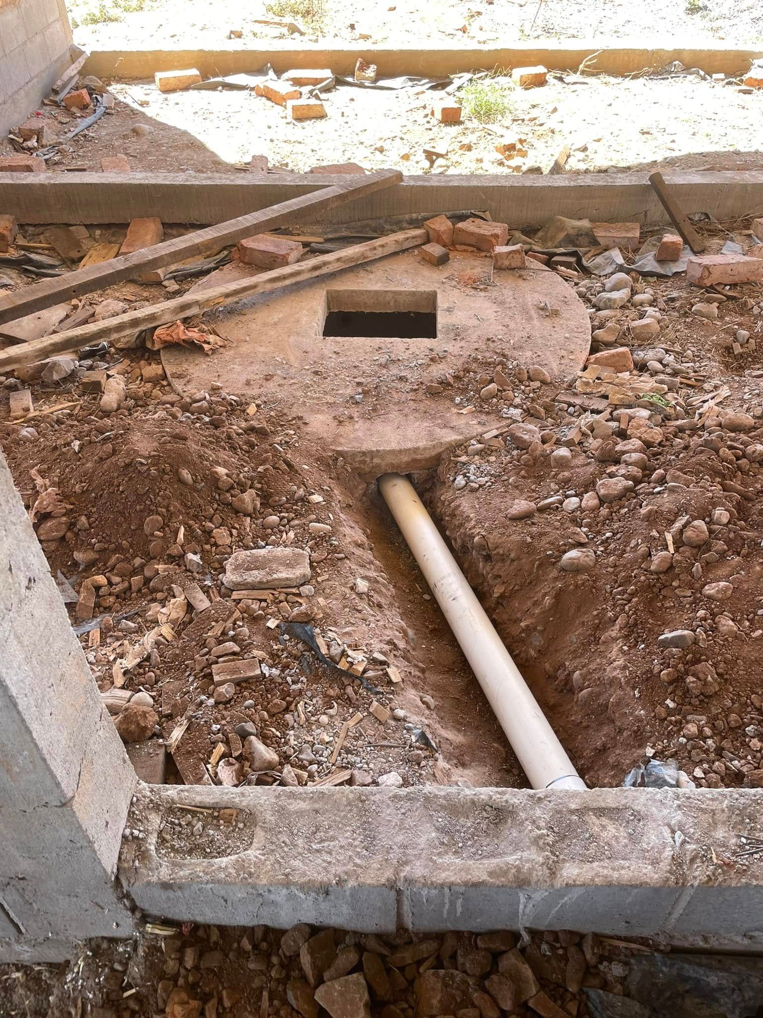 Excavated construction area with a round concrete opening and white pipe amid rubble and dirt