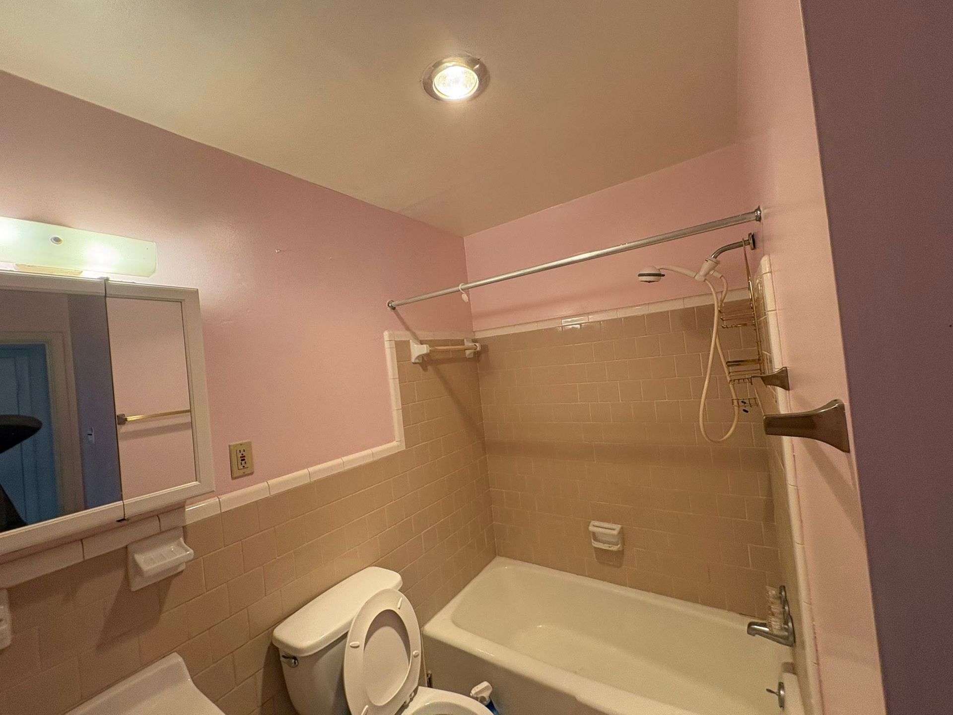 Pink bathroom with a toilet, bathtub, and beige tile walls under a ceiling light