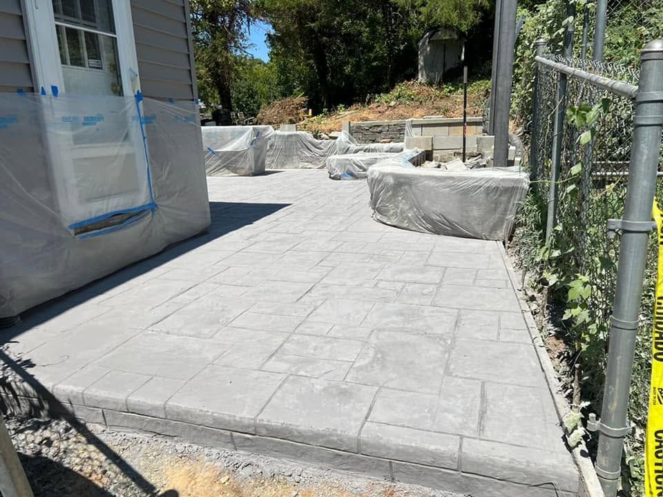 New concrete patio with block edging beside a house, surrounded by landscaping and fence posts