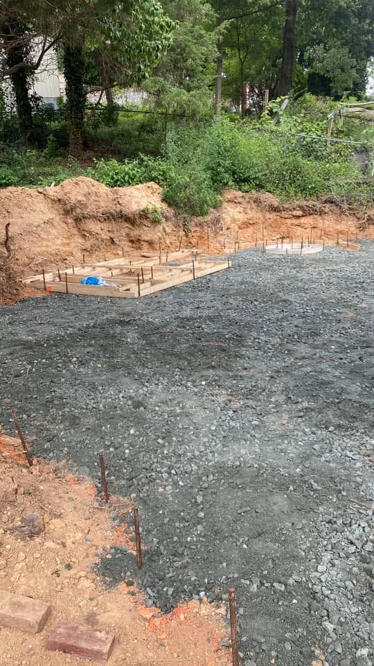 Freshly poured concrete slab beside a dirt trench and green trees at a construction site