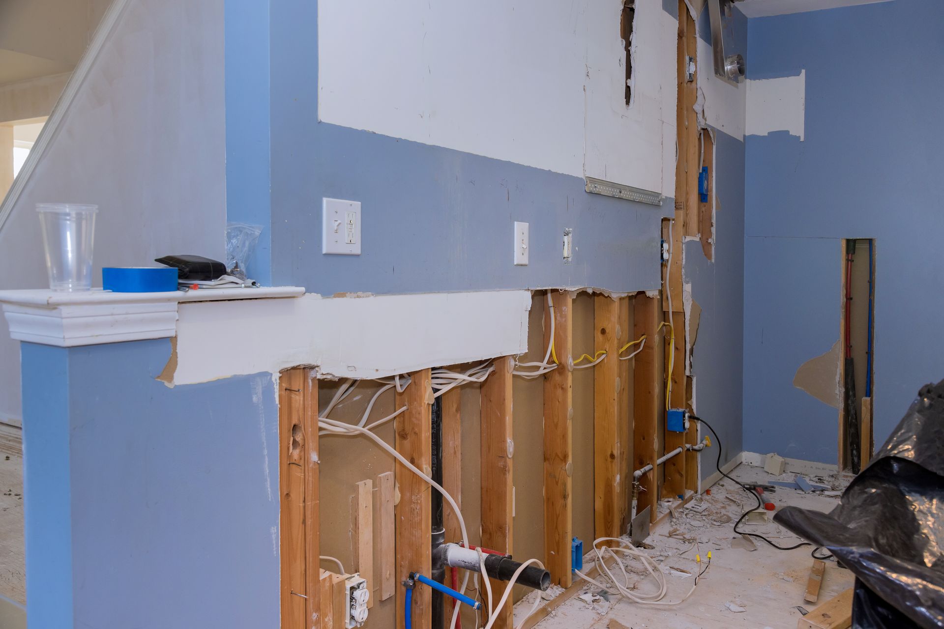 Partially demolished kitchen with exposed studs, debris, and blue walls after renovation or water damage