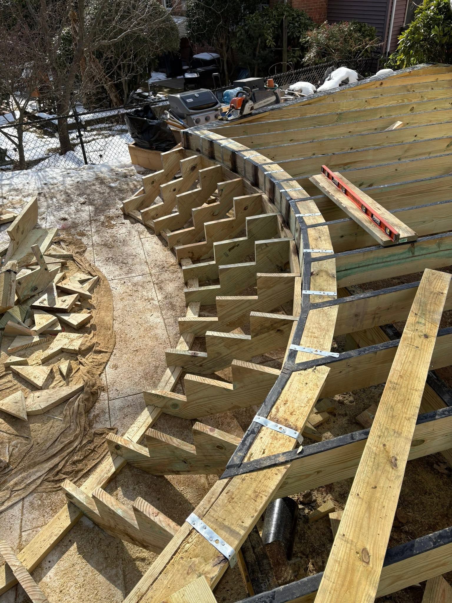Curved wooden retaining wall under construction on a snowy hillside, with scaffolding and lumber supports
