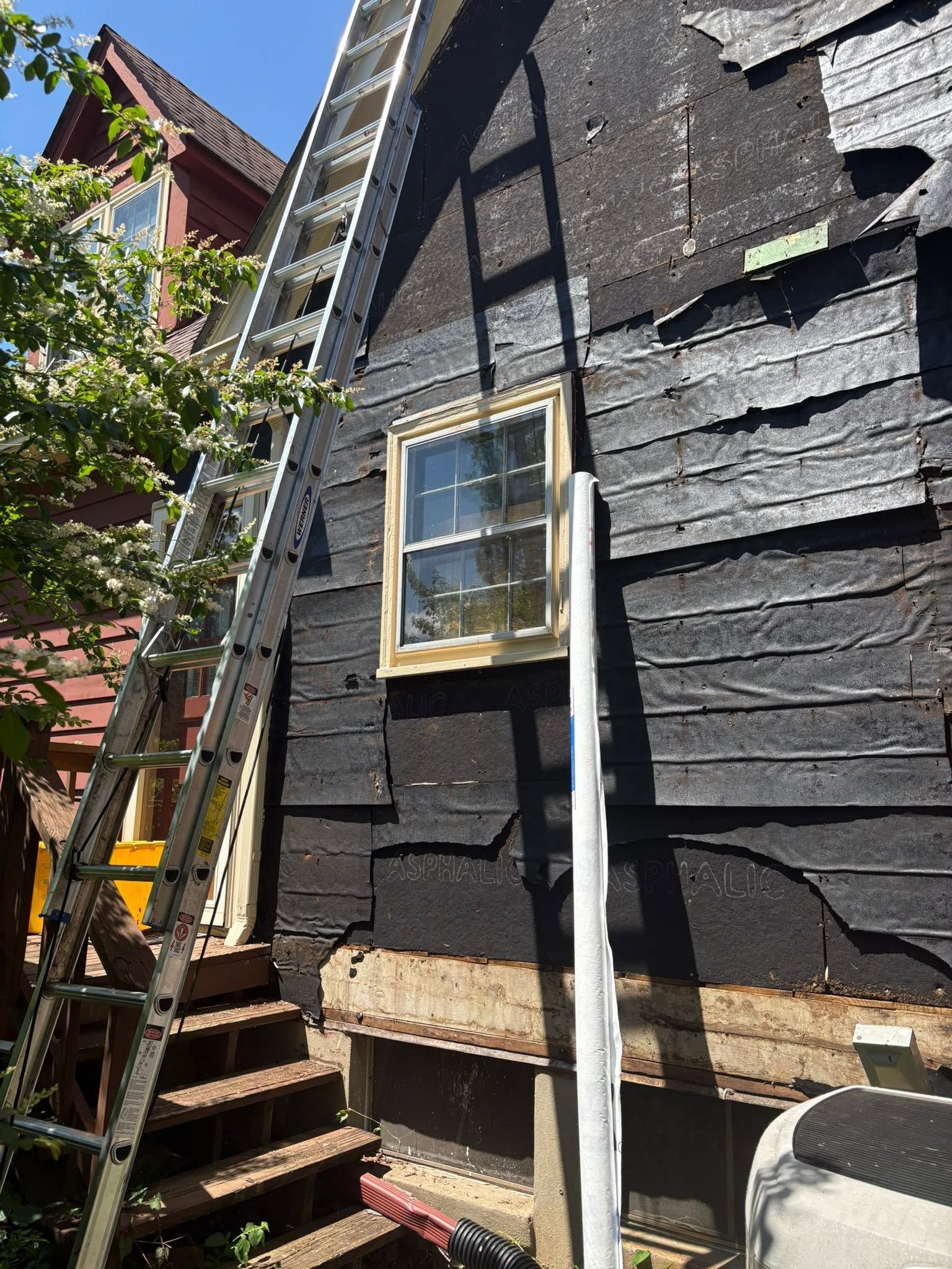 Black house exterior with ladder, small window, and exposed siding during repairs