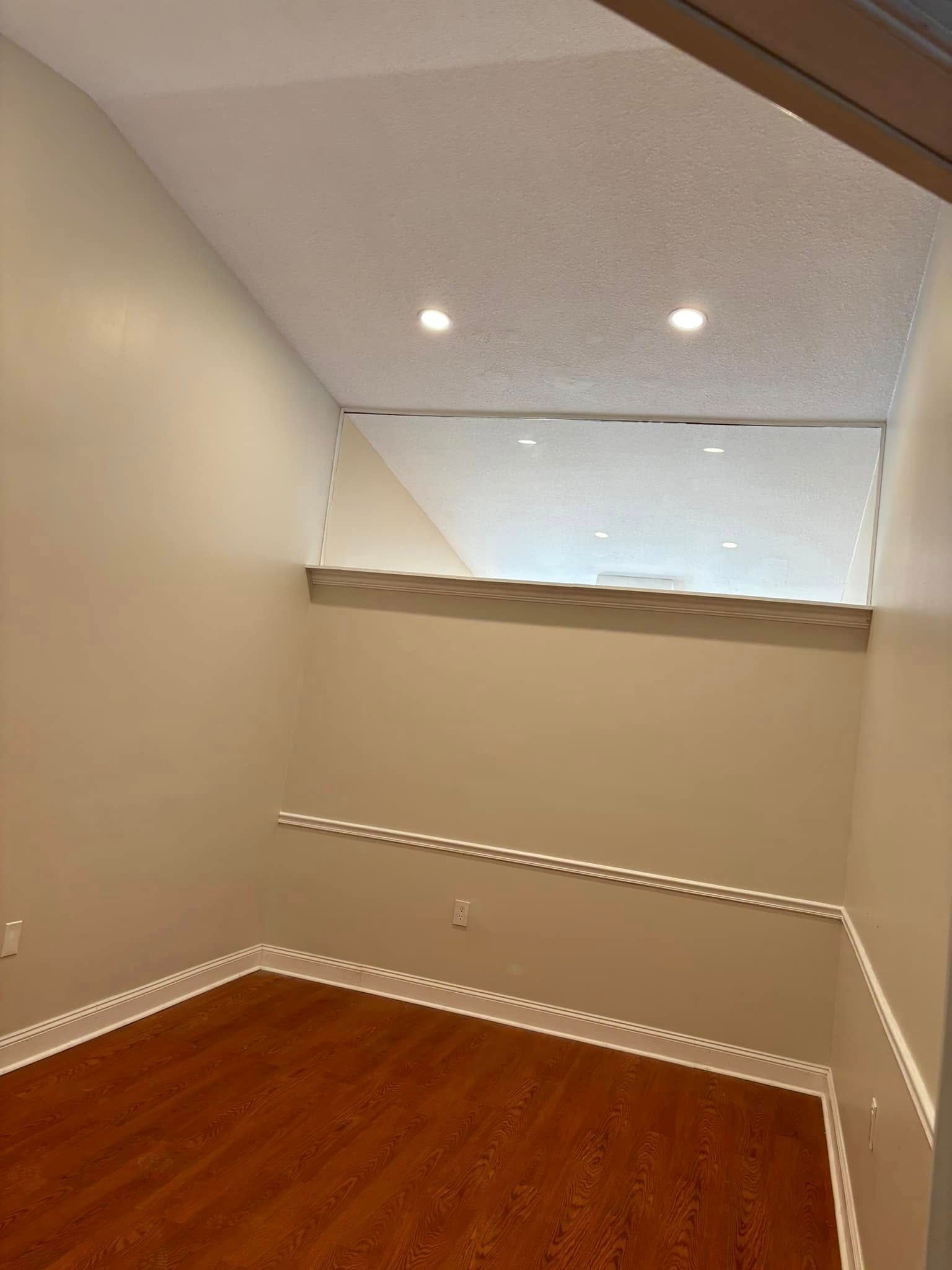 Empty beige closet or small room with wood floor, slanted ceiling, and recessed lights.