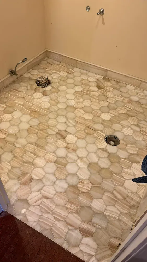 Small bathroom with a hex-tile floor, toilet flange and drain openings, under renovation