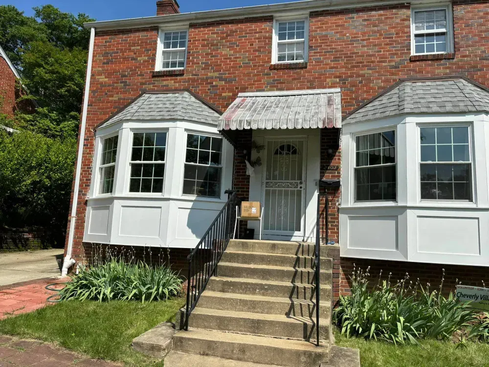 Brick house with white bay windows, front steps, and a covered porch with hanging lace canopy.