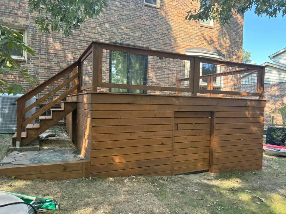 Wooden backyard deck with stairs, railing, and lattice skirting beside a brick house
