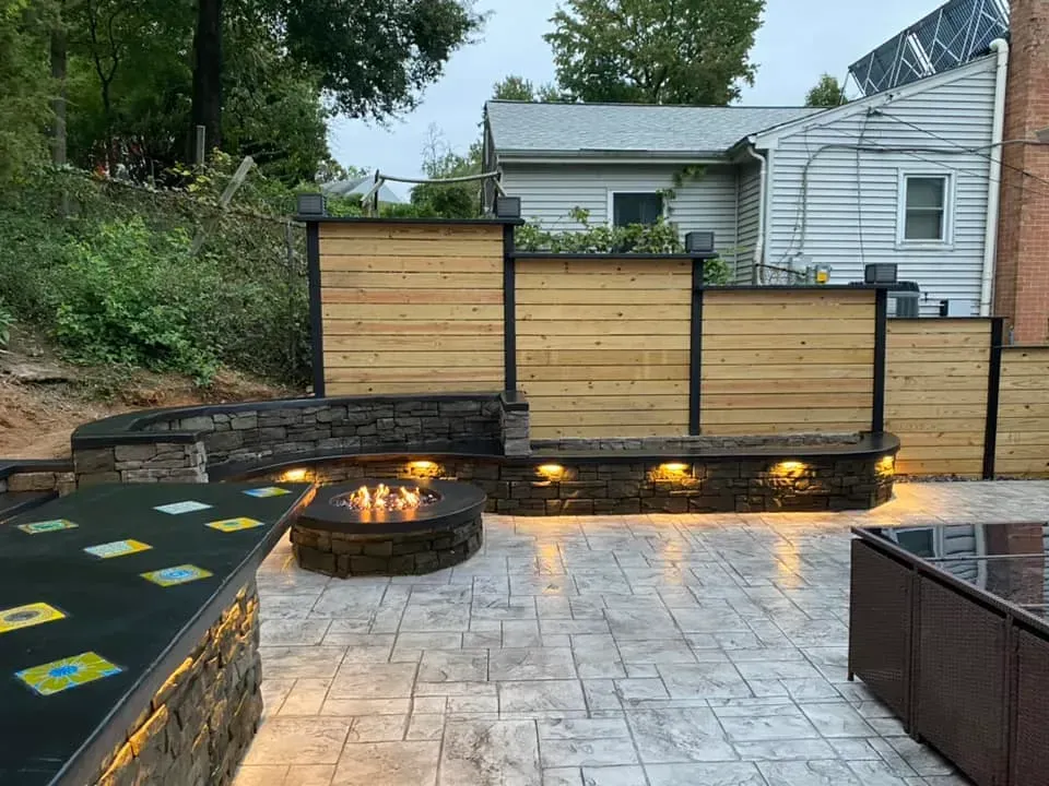 Backyard patio with circular fire pit, wood privacy fence, and wet stone pavers beside a house