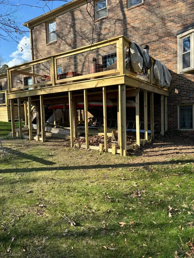 Wooden deck and support posts attached to a brick house in a grassy yard